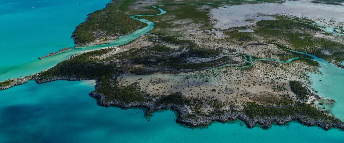 An aerial view of a coastal area with clear turquoise waters, a winding river, and a mix of sandy and vegetated land.