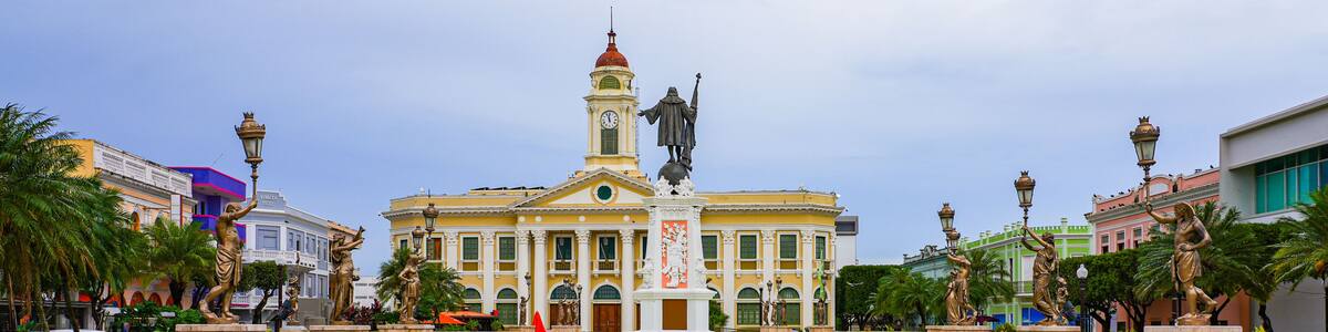 A historic building with a clock tower, surrounded by palm trees and statues.