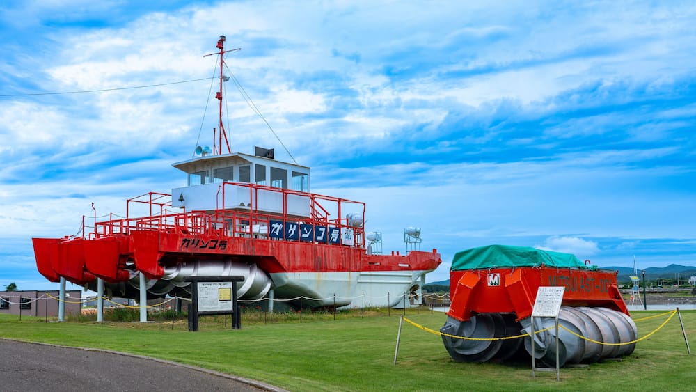 A red and white boat with a cabin, a large red crane, and a green tarp on the ground.