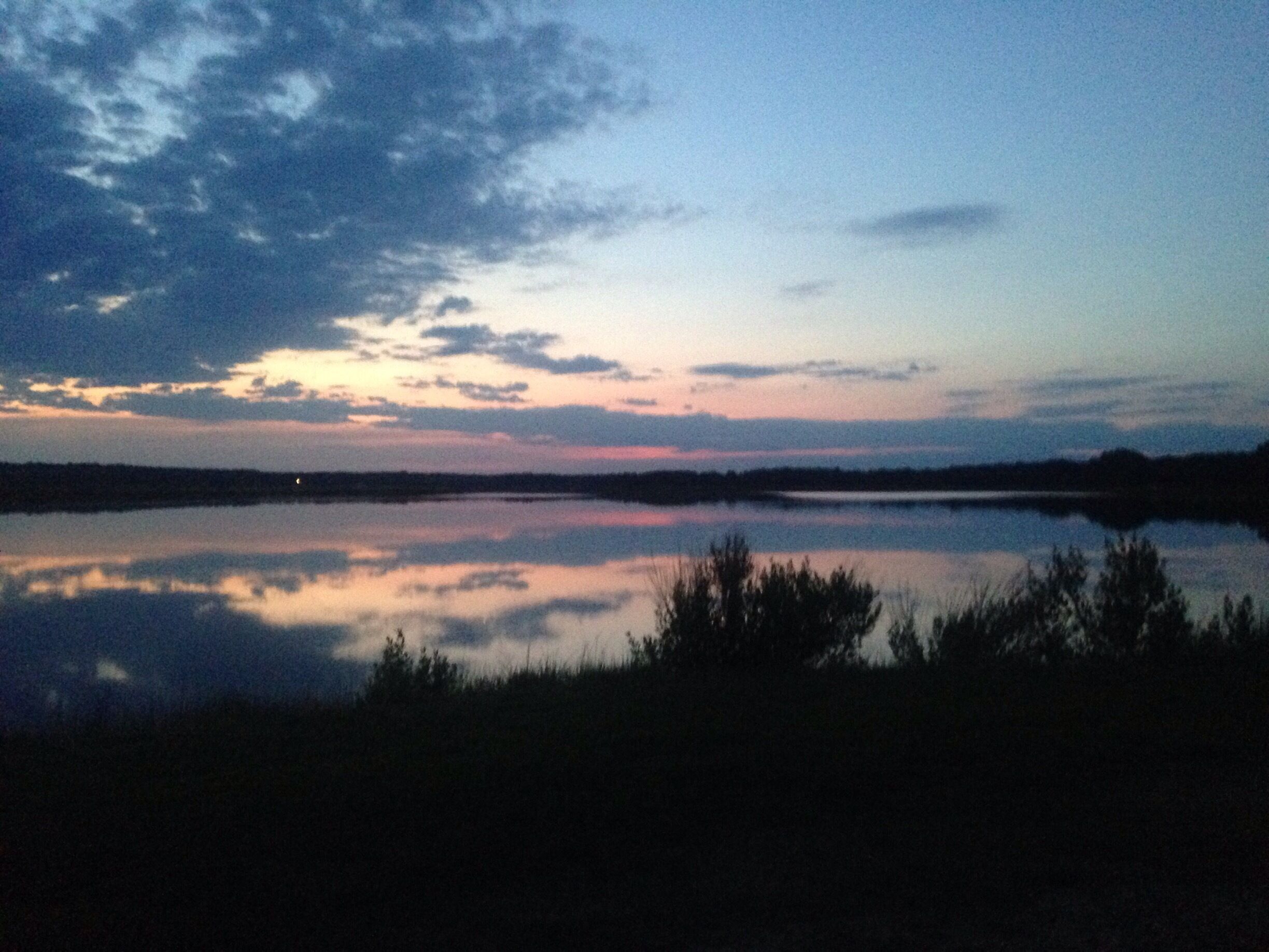 A calm lake at dusk with a clear reflection of the sky.