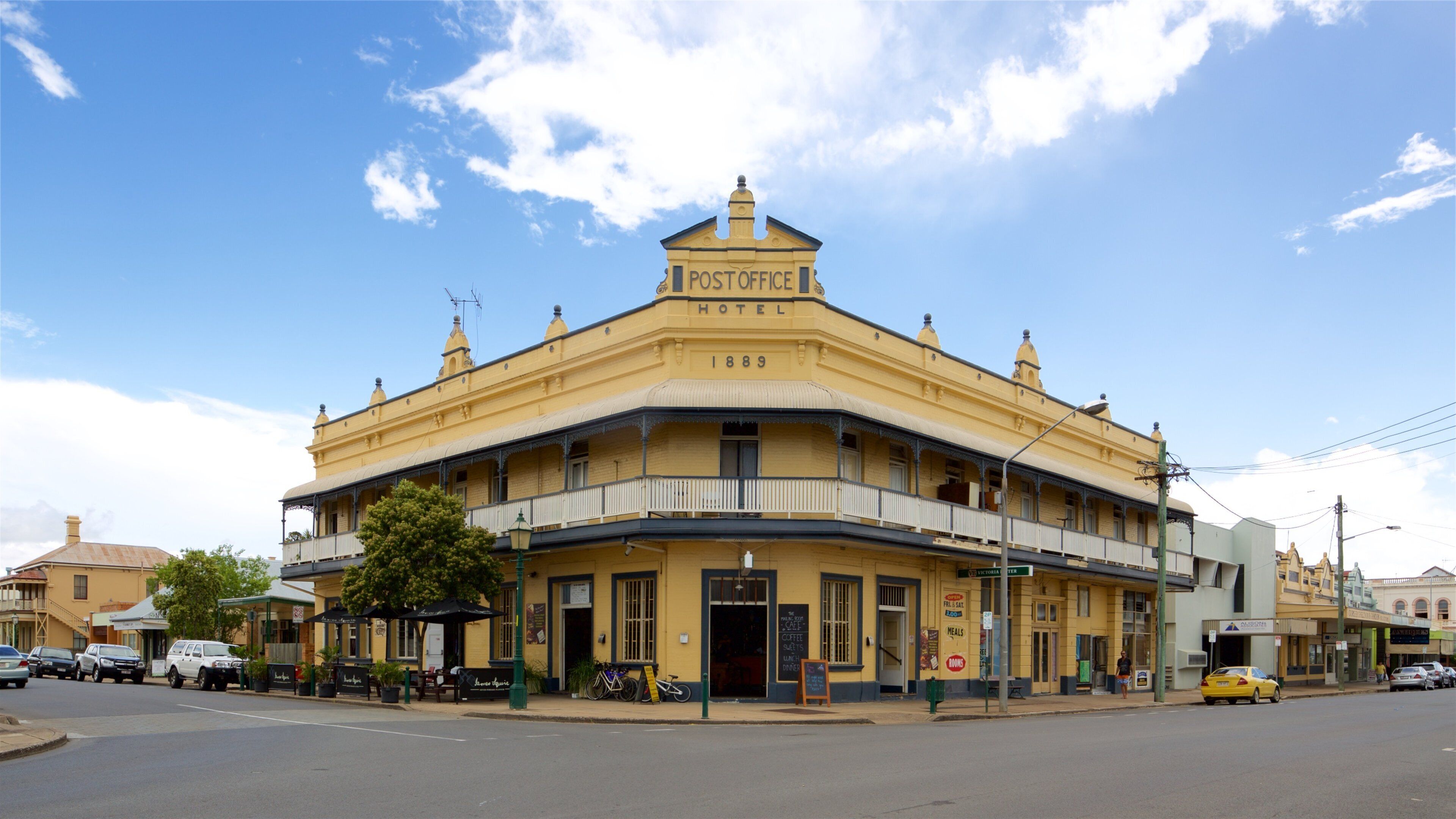 A yellow building with a balcony and a sign that reads "POST OFFICE HOTEL 1889".