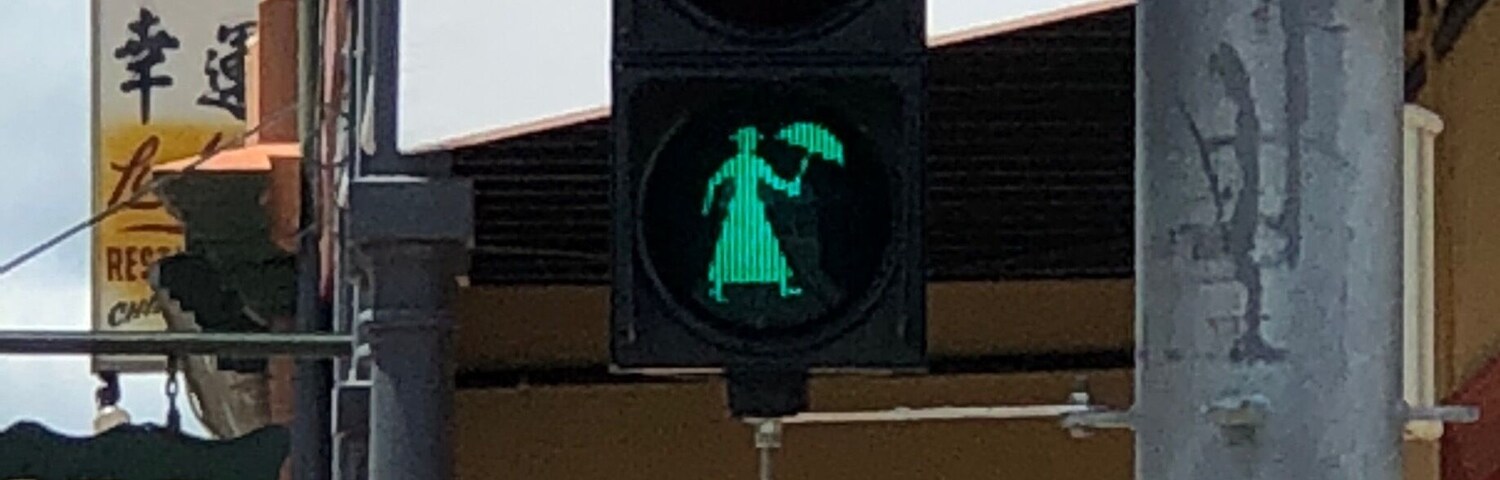 Un feu de signalisation avec un signal pour les piétons, un panneau vert portant le mot « Francis » et un drapeau rouge portant le mot « Patio ».