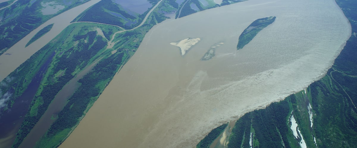 A river winding through a green landscape with patches of water and a cloudy sky above.