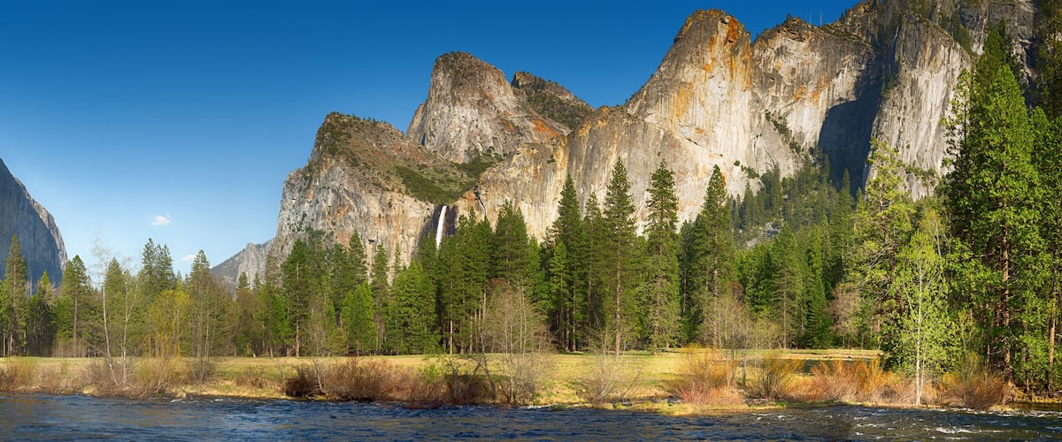 A river flowing through a forest with tall, rugged mountains in the background.