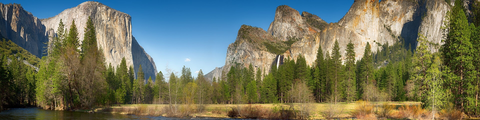 A river flowing through a forest with tall, rugged mountains in the background.
