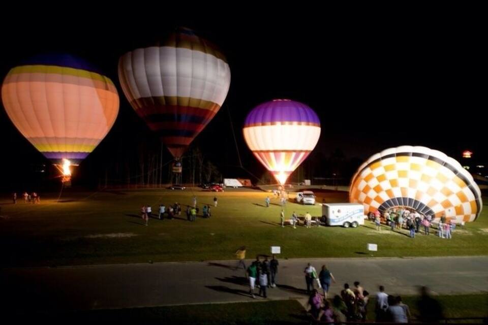 Globos aerostáticos de noche con gente reunida alrededor.