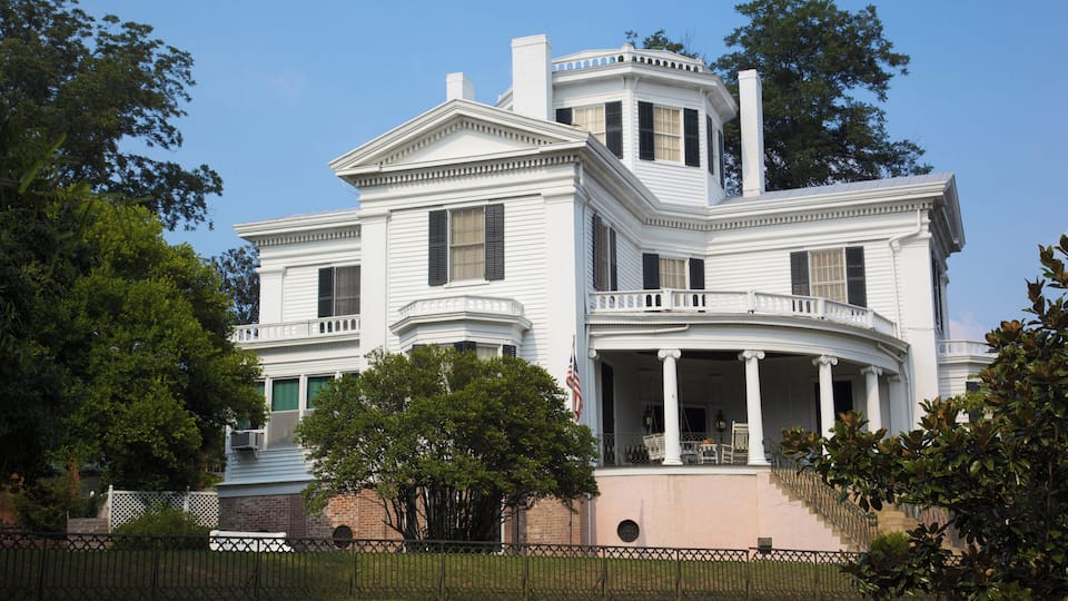 A large white house with a wrap-around porch and columns.