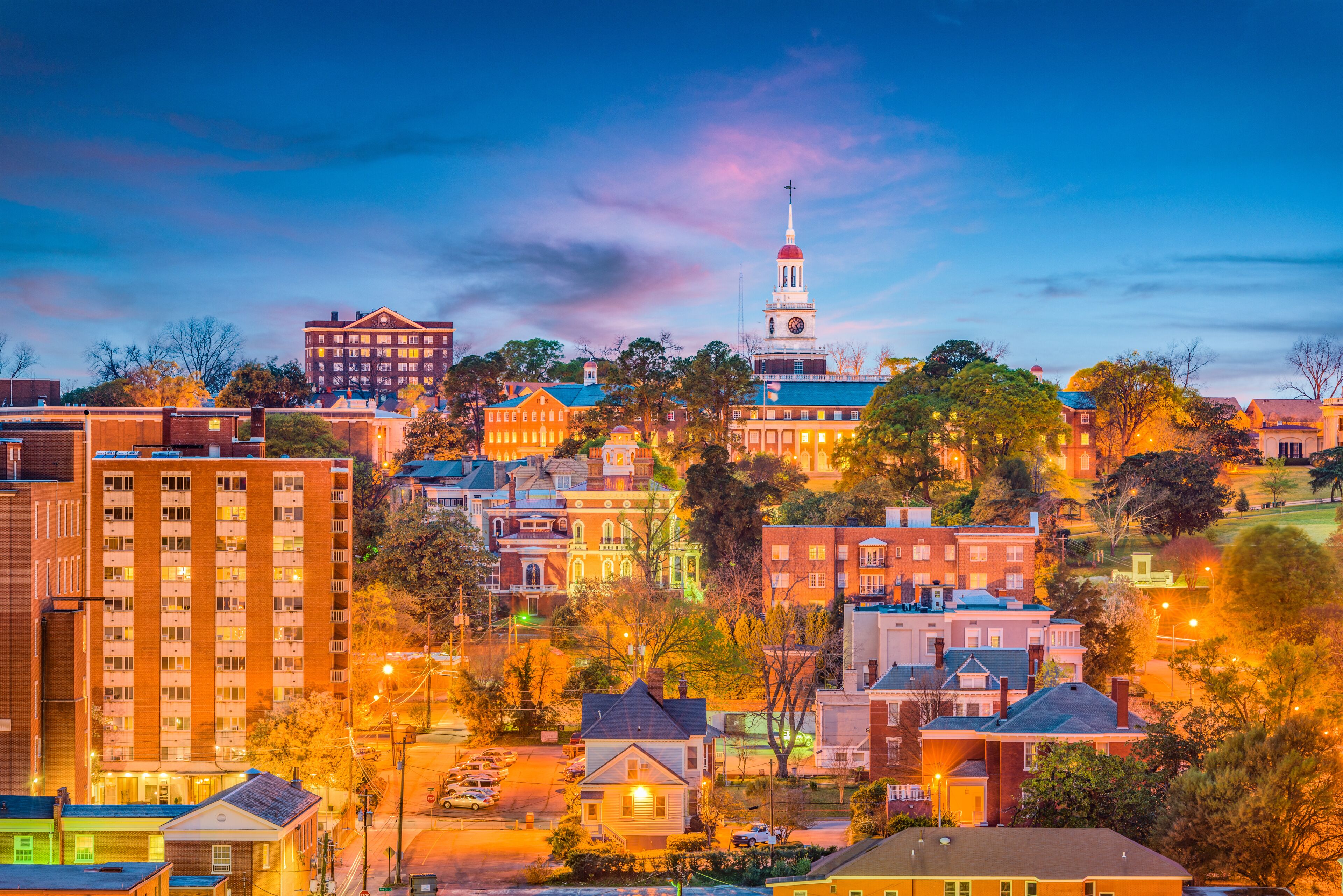 A cityscape with a prominent clock tower, various residential and commercial buildings, and a hilly backdrop.