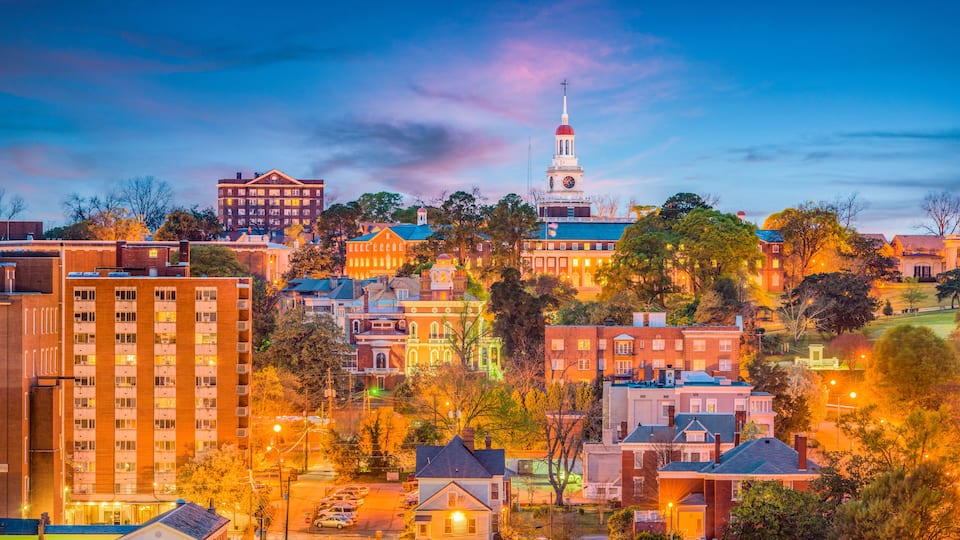 A cityscape with a prominent clock tower, various residential and commercial buildings, and a hilly backdrop.