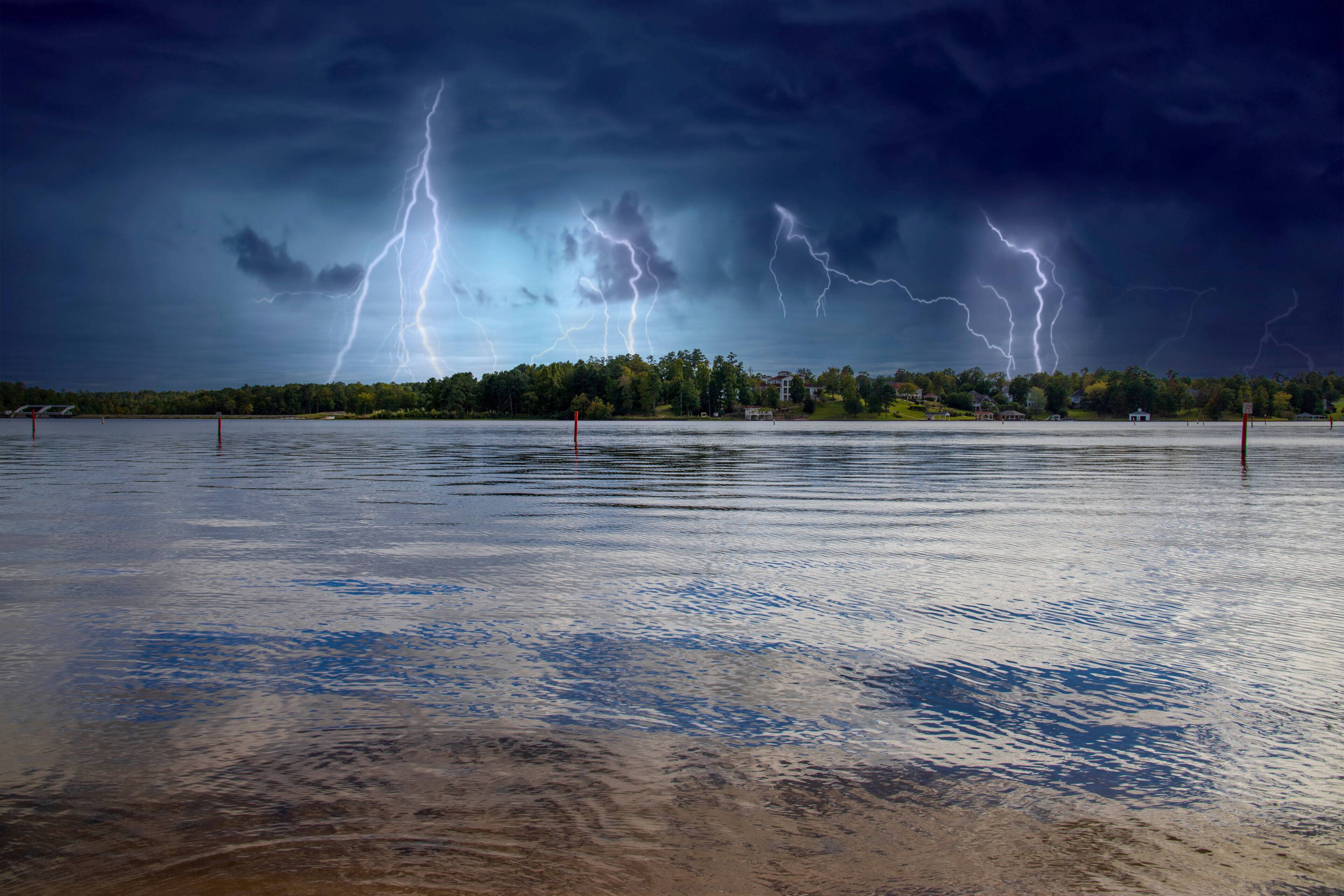 A stormy lake with lightning strikes and a forested shoreline.