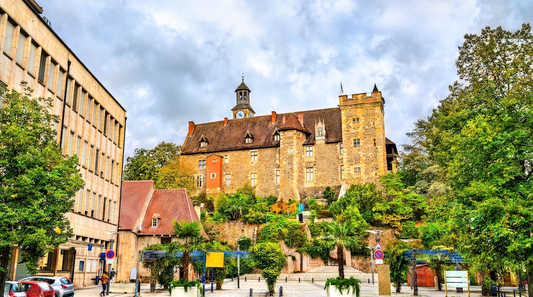 Un bĂątiment historique dotĂ© dâune tour horloge, entourĂ© dâune vĂ©gĂ©tation luxuriante et bordĂ© dâune place dallĂ©e.