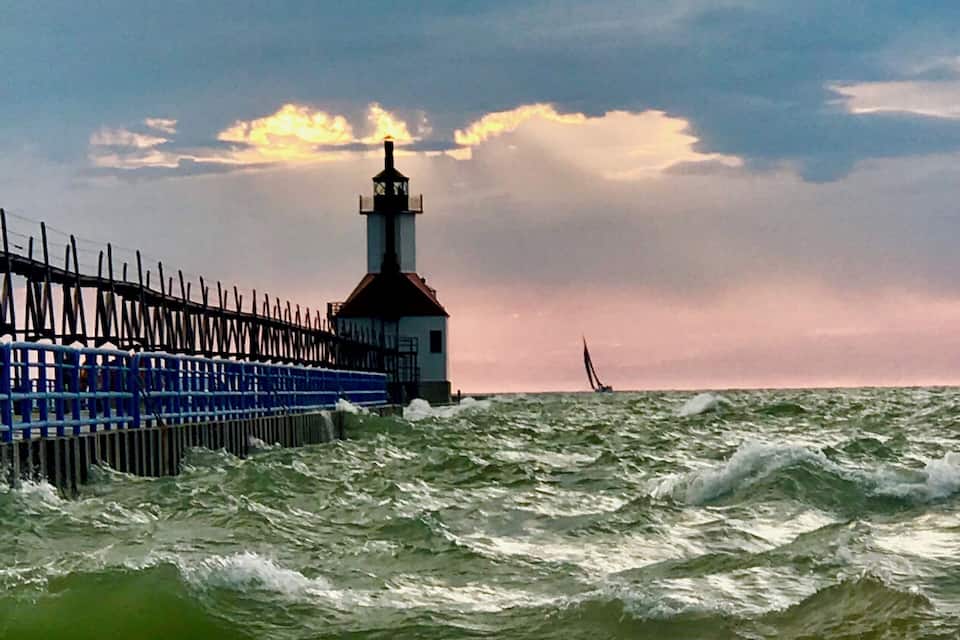 A lighthouse, rough sea, and a seagull on a sandy beach.