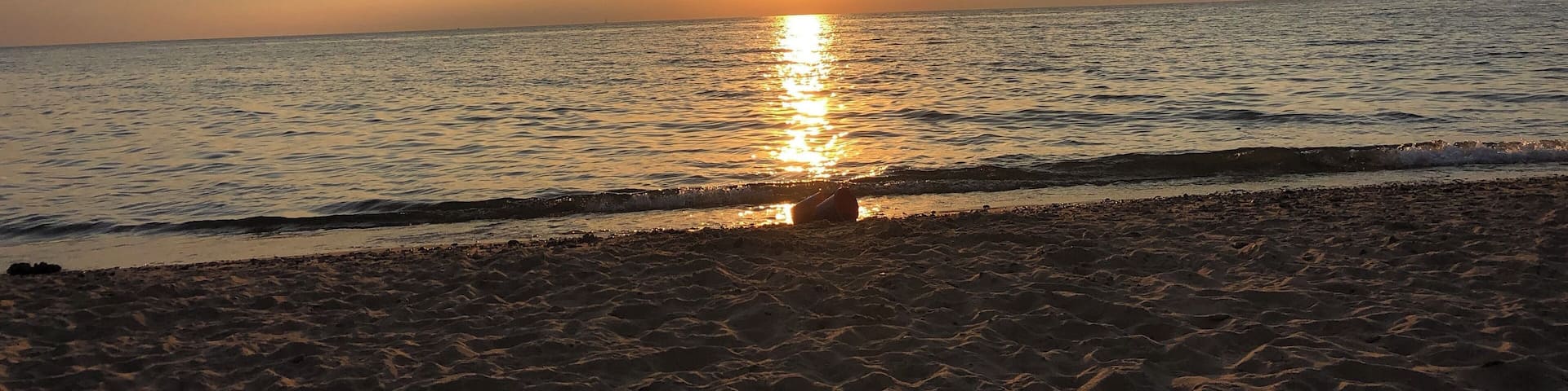 Un atardecer sobre una playa con el sol reflejándose en el agua.