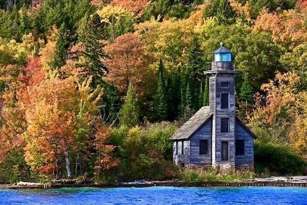 Un phare situé au bord d’une côte bordée d’une forêt aux couleurs automnales.