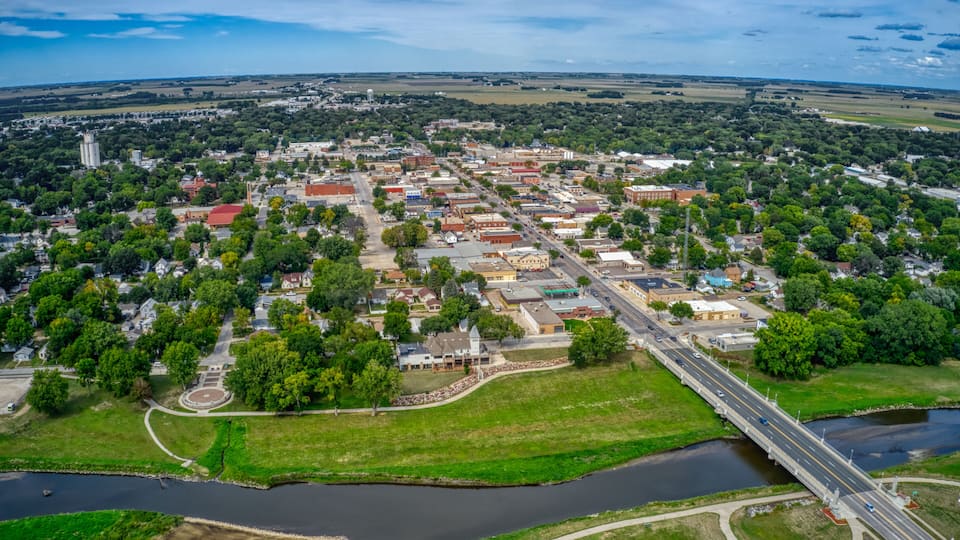 An aerial view of a town with a river, a bridge, and surrounding greenery.