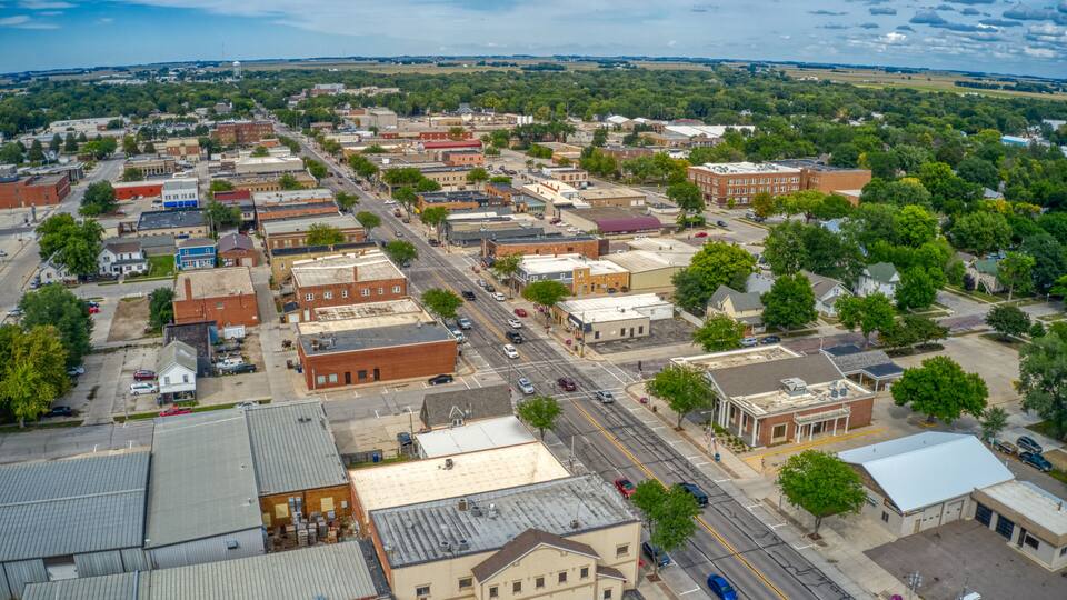 An aerial view of a small town with a grid of streets, various buildings, and surrounding greenery.