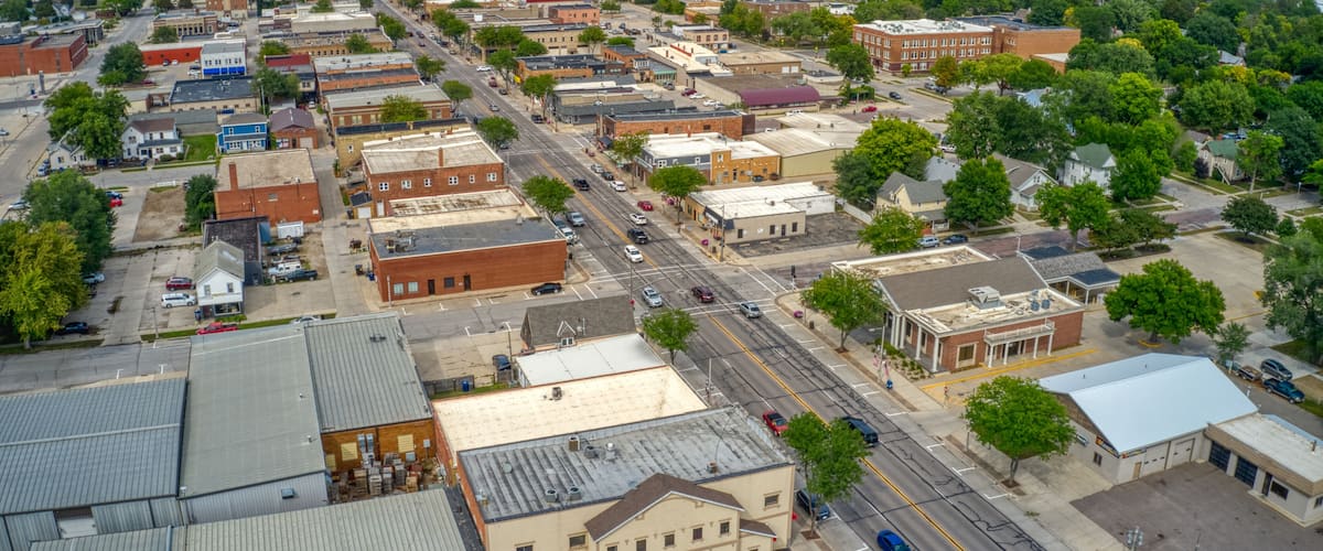 An aerial view of a small town with a grid of streets, various buildings, and surrounding greenery.