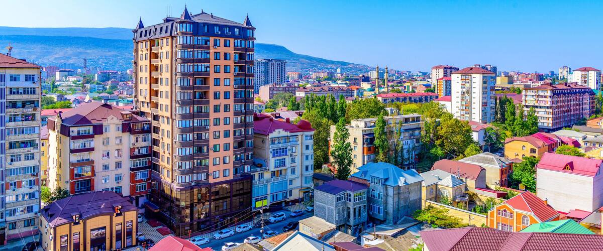 A cityscape with a prominent tall building, colorful residential buildings, and a distant mountain range.
