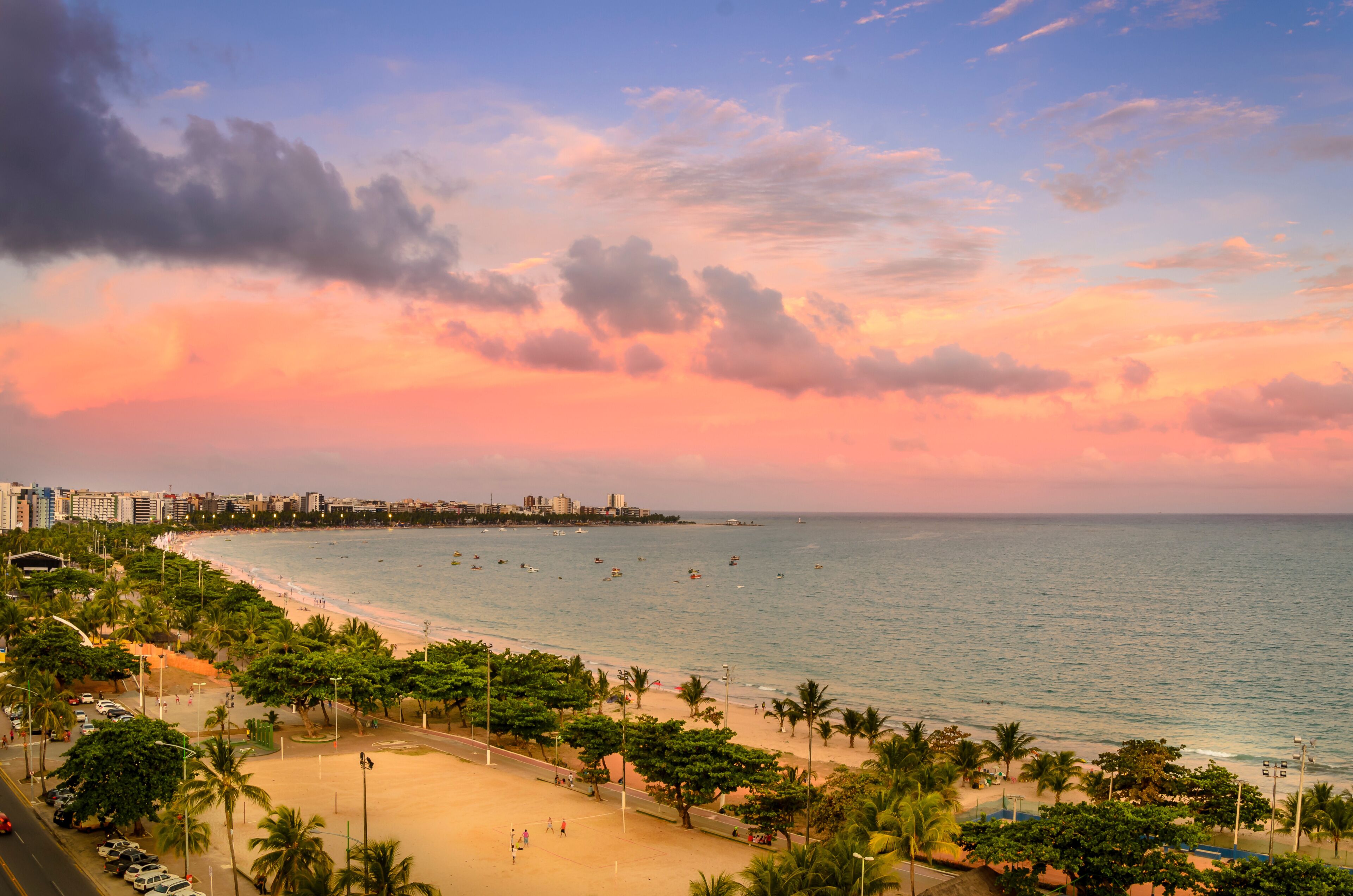 Paisagem costeira com praia, palmeiras e céu ao pôr do sol.