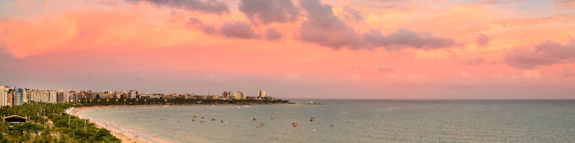 Paisagem costeira com praia, palmeiras e céu ao pôr do sol.