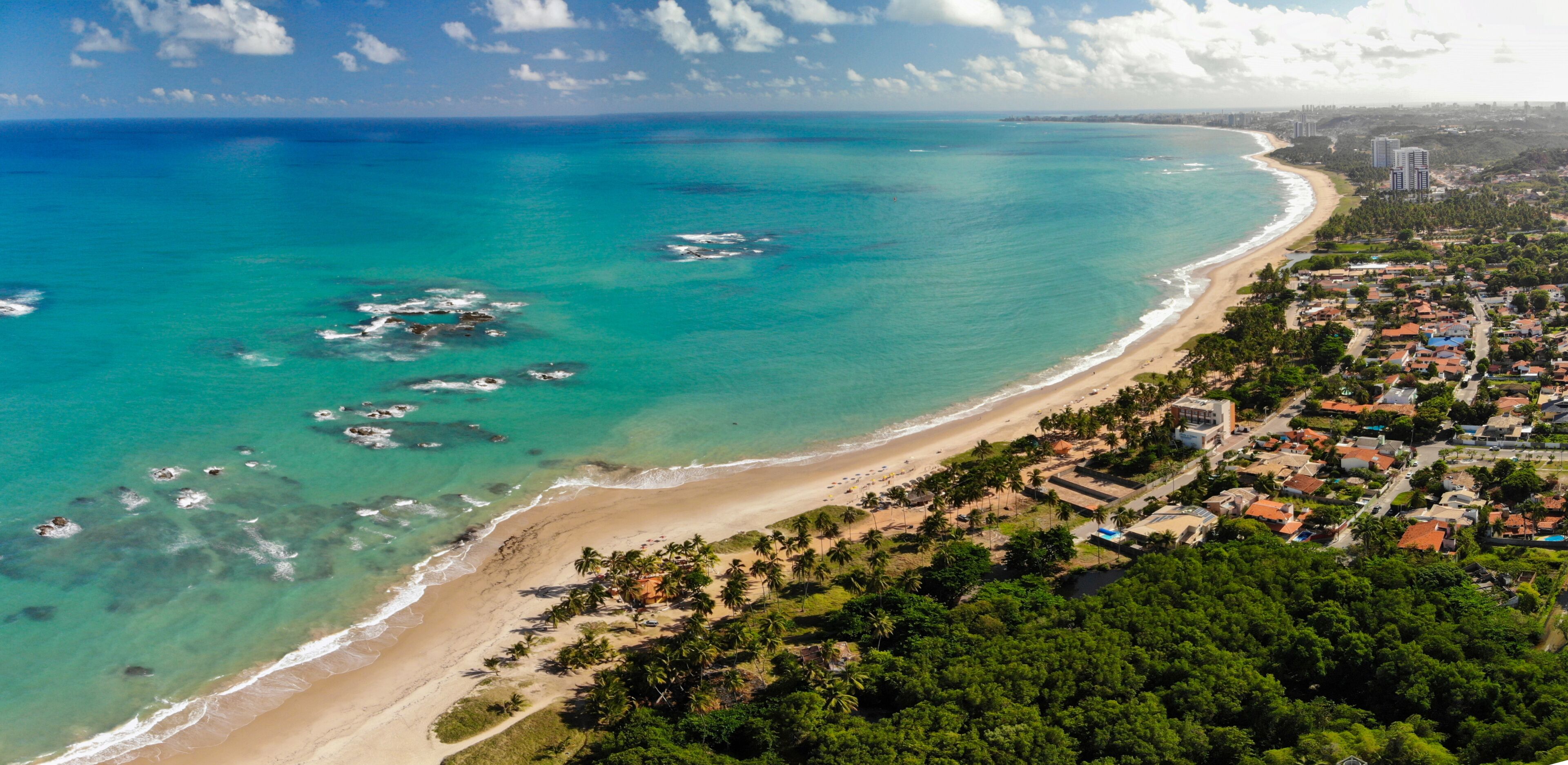 Un pueblo costero con playa, aguas turquesas cristalinas y un bosque verde frondoso.