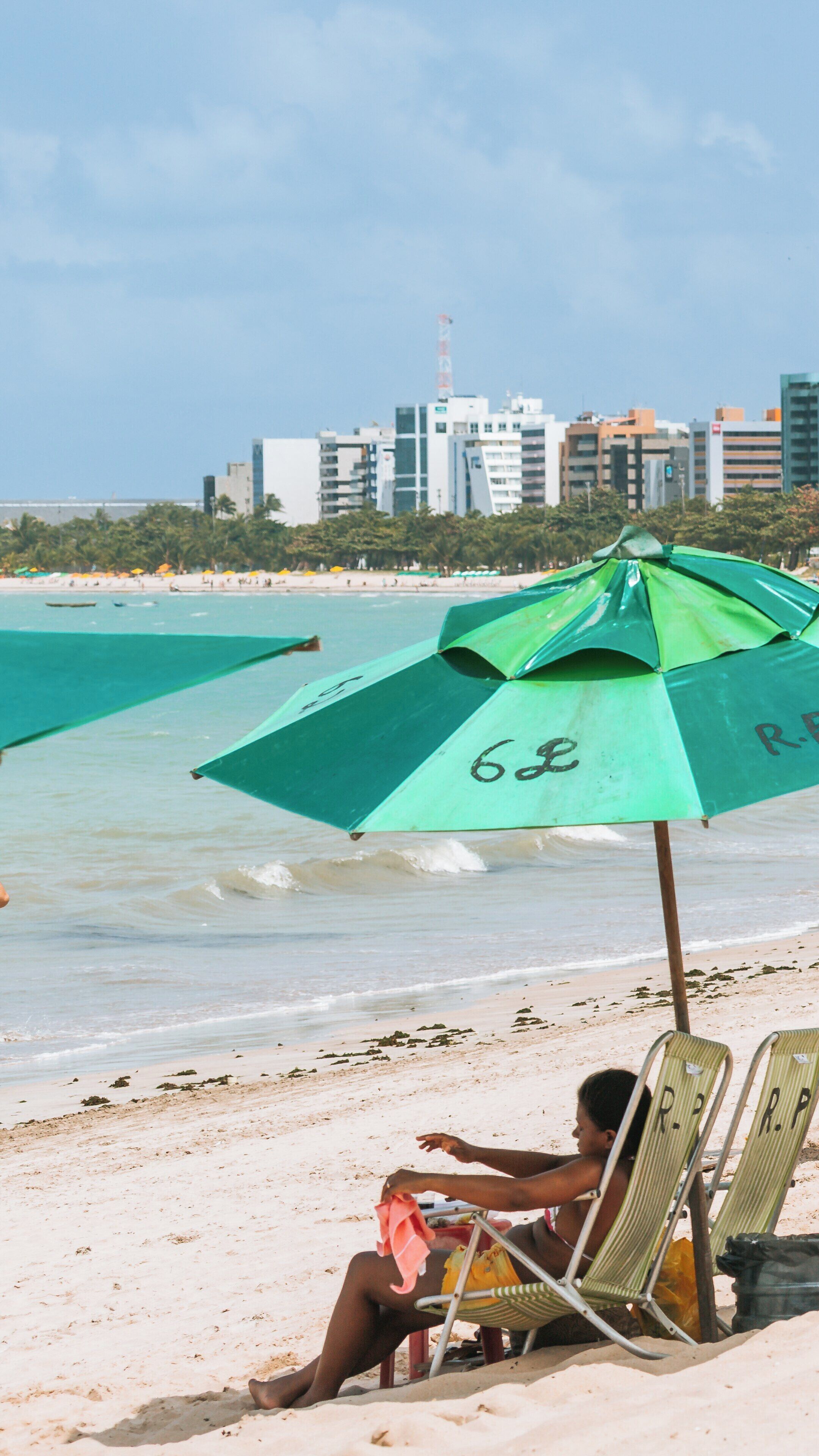 Relaxation at Pajucara Beach with umbrellas and city backdrop in Pajuçara, Maceió, Alagoas, Brazil on a sunny day