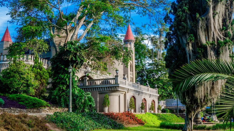 A historic building with red-roofed towers, surrounded by lush greenery and a well-maintained lawn.