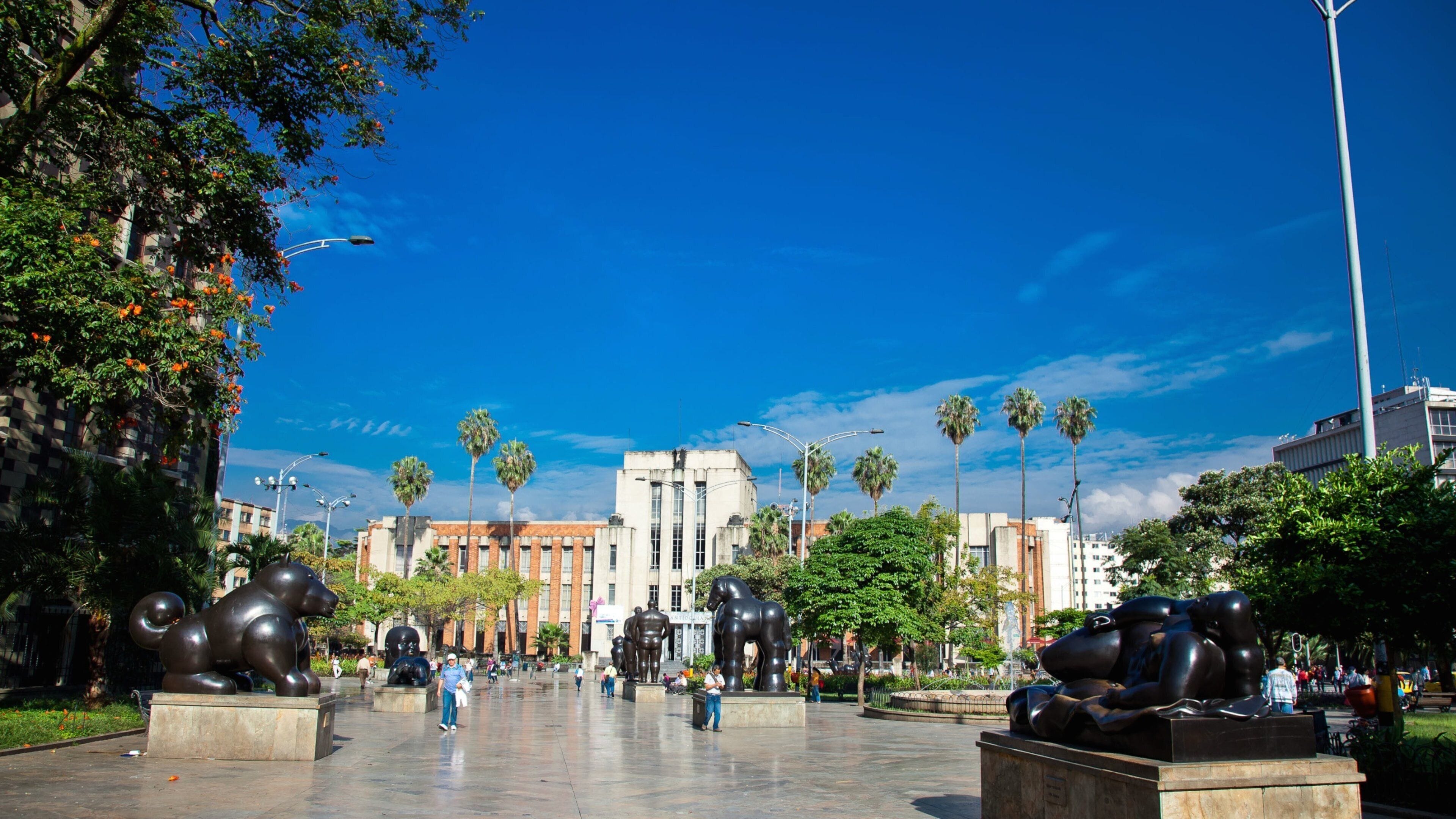 A plaza with large bronze sculptures, palm trees, and a clear blue sky.