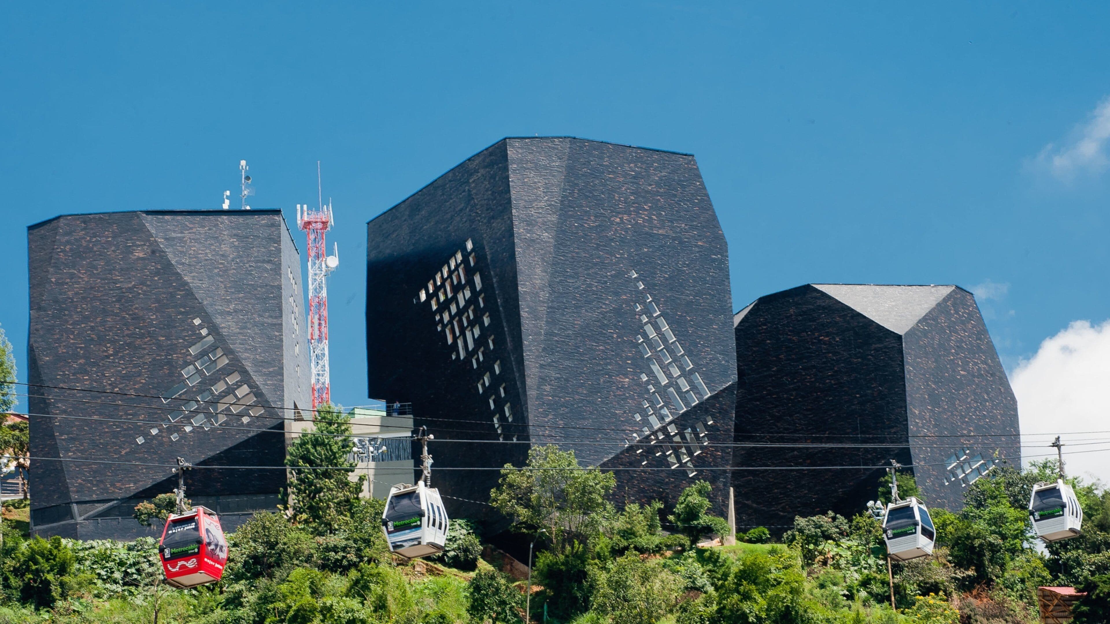 Three large black buildings with geometric patterns, surrounded by greenery and cable cars.