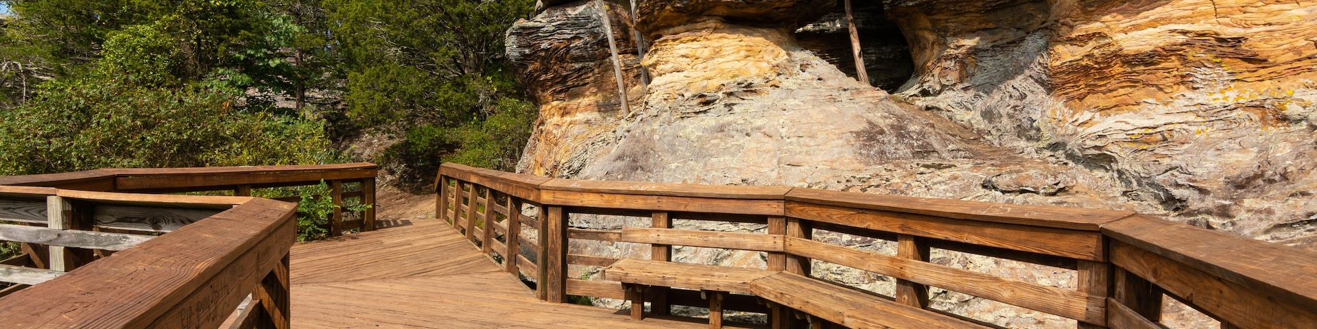 Un muelle de madera que lleva a un promontorio rocoso con bancos.
