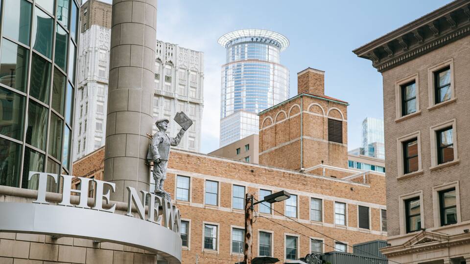 A statue of a man holding a newspaper in front of a building with the sign "THE NEW".