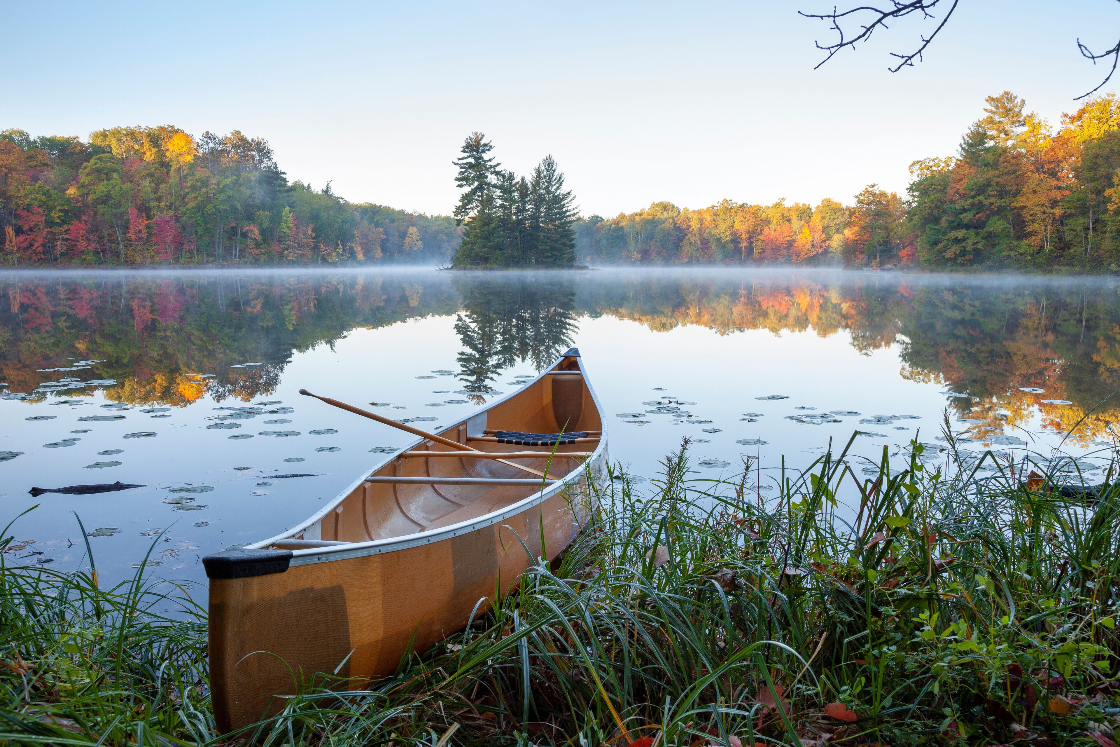 A canoe on a calm lake surrounded by autumn foliage.