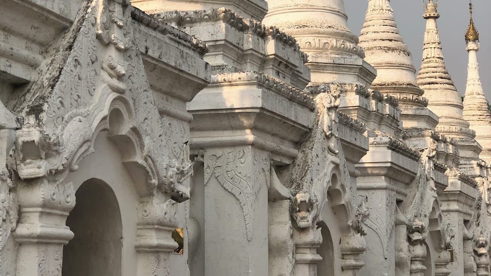 A row of white, intricately carved temple spires with detailed carvings and golden tops.