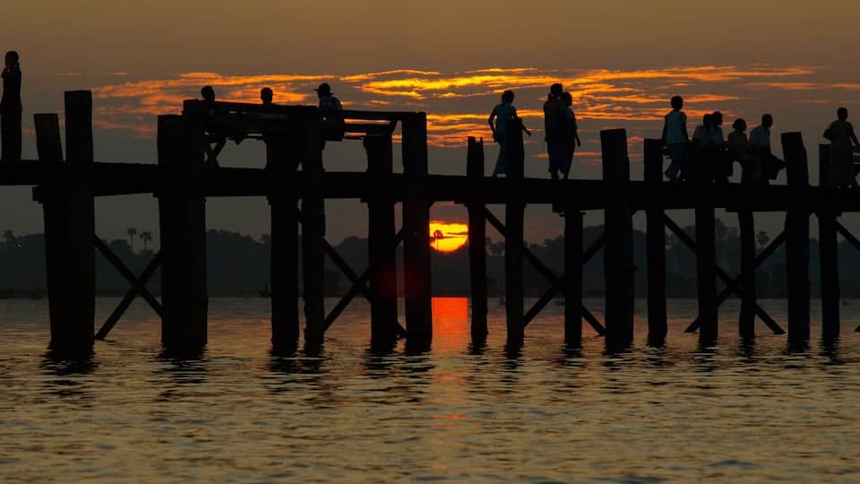 A sunset over a wooden pier with people silhouetted against the sky.