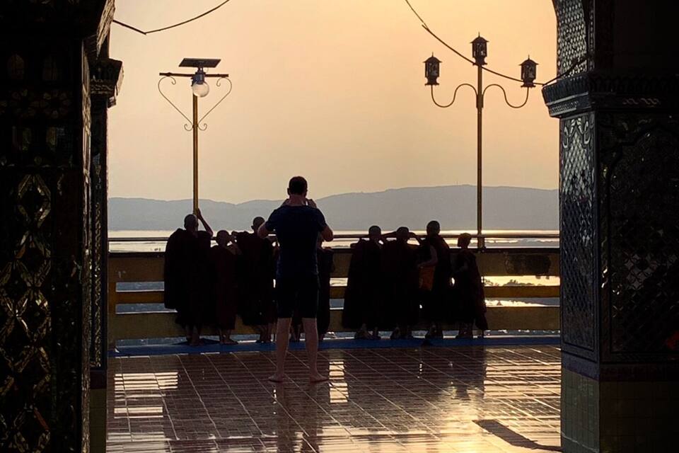 A sunset over a body of water, viewed through an ornate archway with tiled flooring.