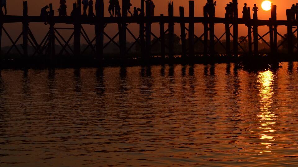 A sunset over a pier with people silhouetted against the sky.