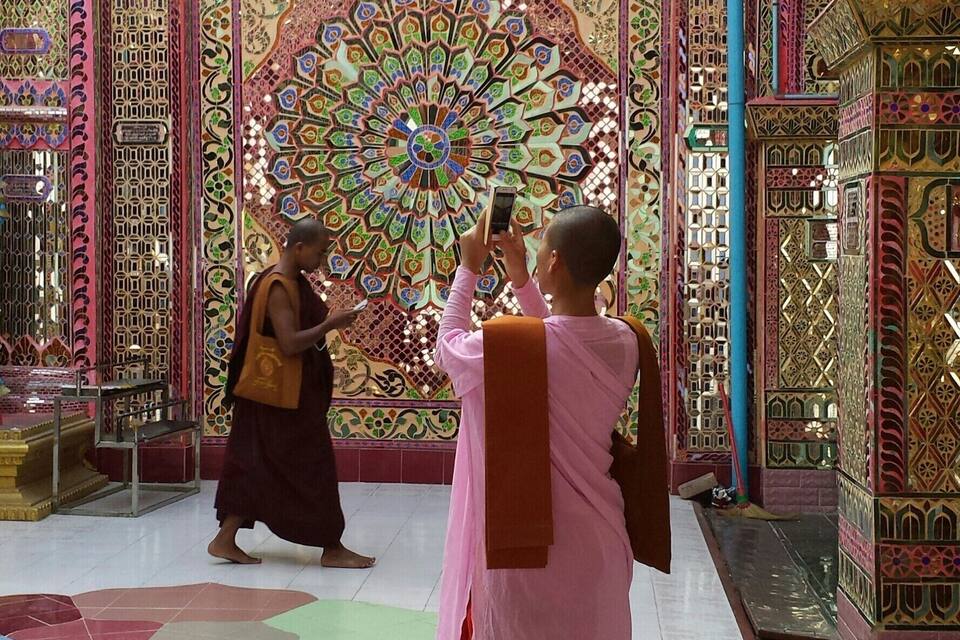 A person taking a photo of a colorful, intricately designed wall with geometric patterns and a central circular motif.