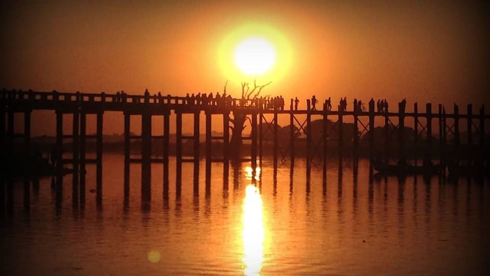 A sunset over a wooden pier with people silhouetted against the sky.