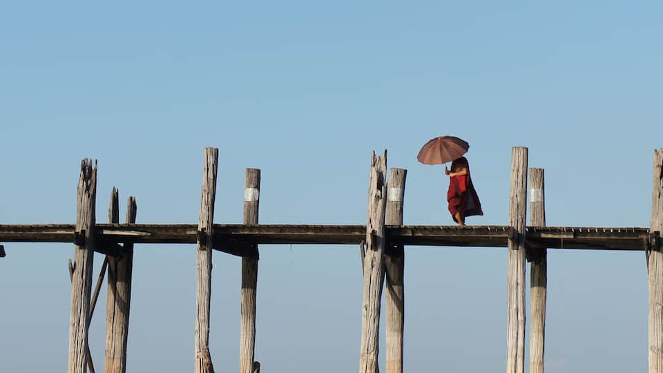 A person walking on a wooden bridge with a brown umbrella.