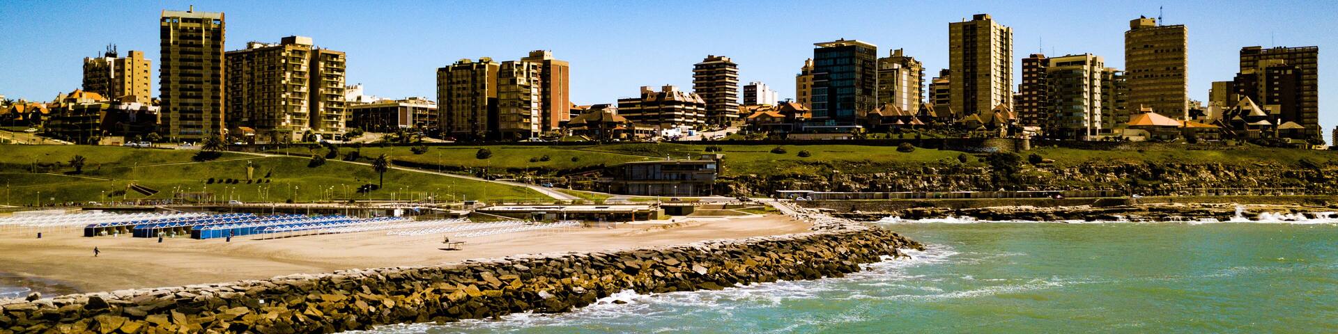 A coastal cityscape with high-rise buildings, a sandy beach, and a rocky shoreline.