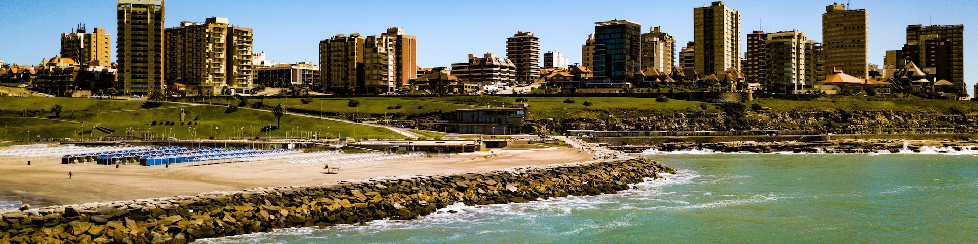 Un paisaje urbano costero con edificios altos, una playa de arena y un litoral rocoso.