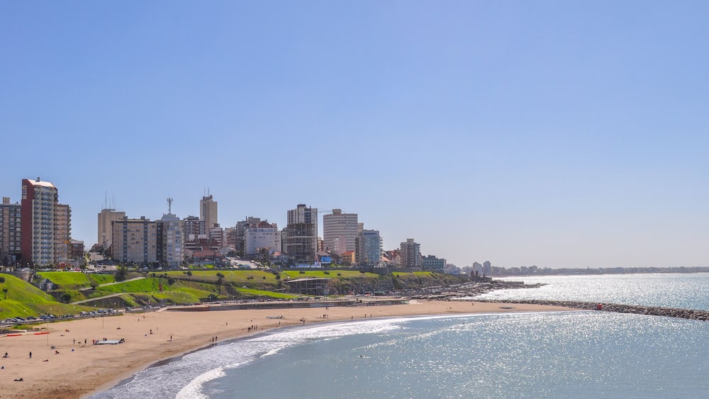 A coastal cityscape with a beach, green hills, and high-rise buildings.