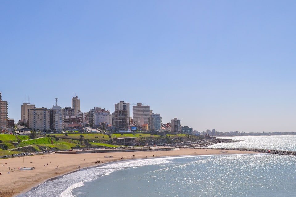 A coastal cityscape with a beach, green hills, and high-rise buildings.