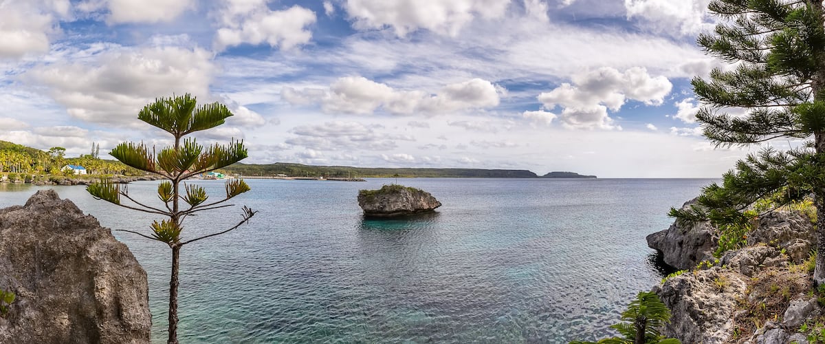 A coastal landscape with rocky outcrops, clear blue water, and lush greenery.