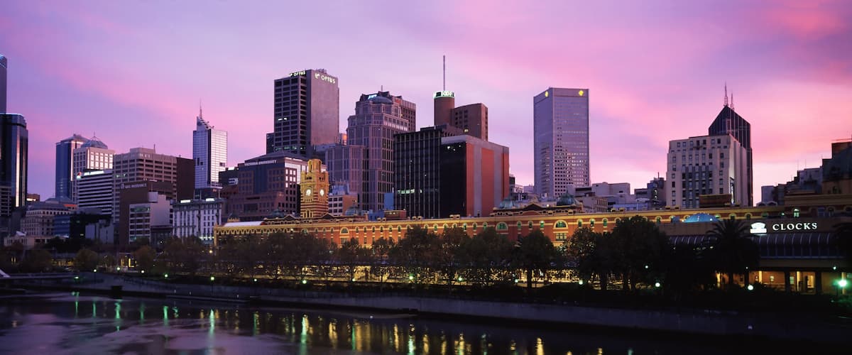 A city skyline with modern buildings and a historic clock tower reflecting on the water.