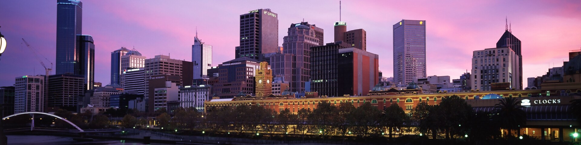Horizonte urbano com edifícios modernos e um antigo campanário refletindo na água.