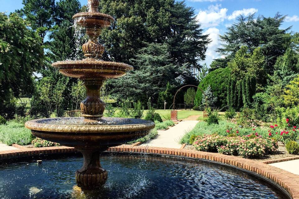A multi-tiered fountain in a garden with a brick pathway and lush greenery.
