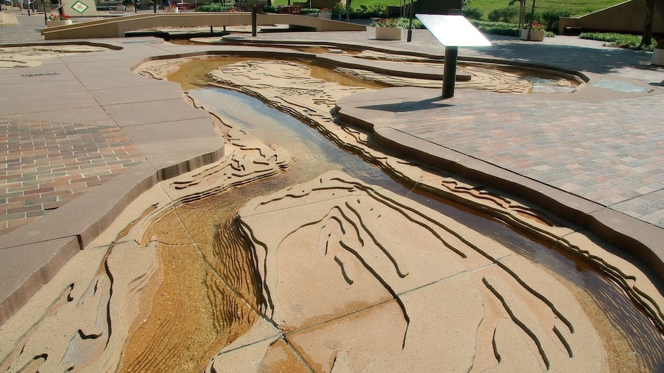 A water feature with a flowing design, surrounded by a paved walkway and benches.