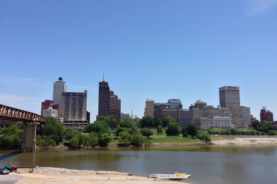 A city skyline with modern buildings, a river, and a park with trees.