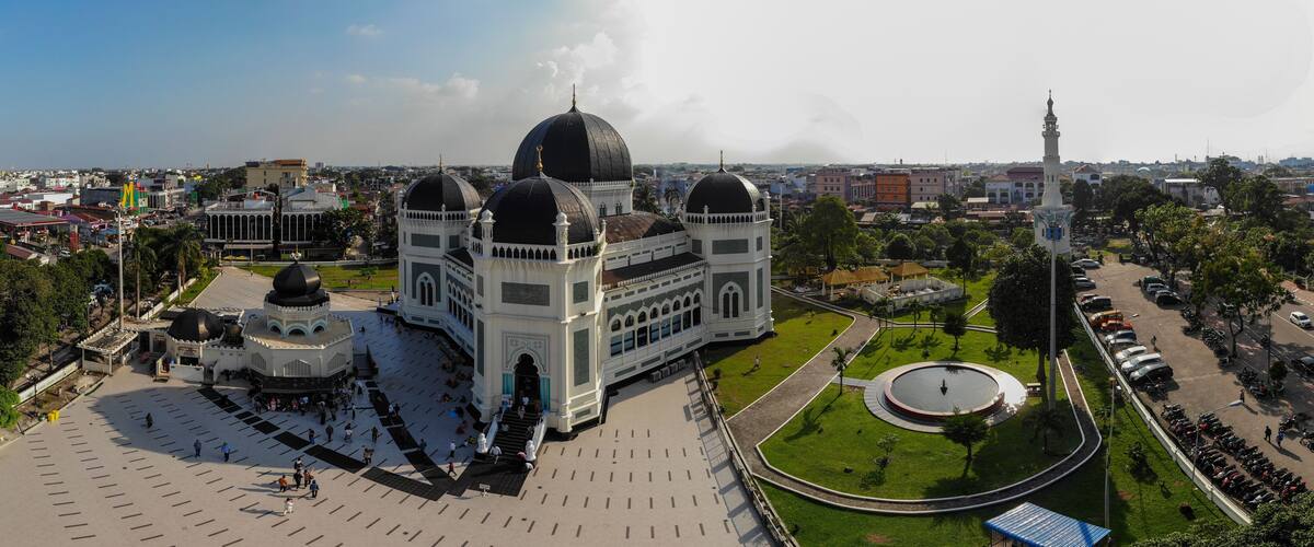 A large mosque with multiple domes and a minaret, surrounded by a spacious courtyard and greenery.